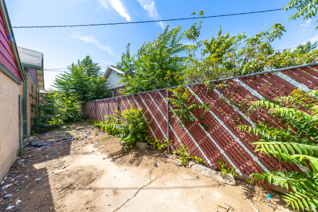193 Locust Street Clearfield, UT 84015 - Photo 29 of 29 Exterior side yard space with a combination of concrete and dirt ground cover, featuring a red and white privacy fence and mature green foliage