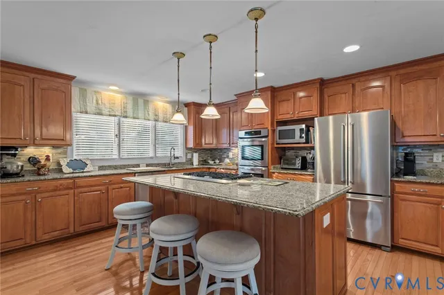 a kitchen with stainless steel appliances granite countertop a sink a stove a refrigerator and wooden floor