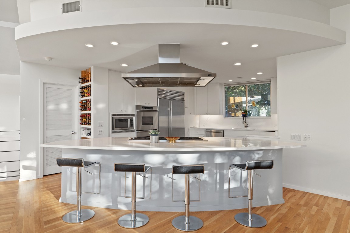 2102 North Oak Canyon Road Austin, TX 78746 - Photo 10 of 40 a kitchen with stainless steel appliances kitchen island granite countertop a table chairs in it and wooden floors