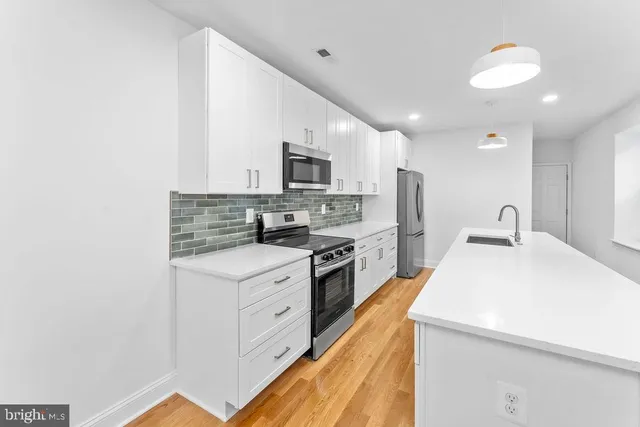 a large kitchen with stainless steel appliances a stove a sink dishwasher and a refrigerator with wooden floor