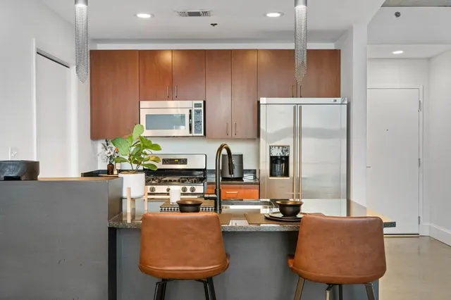 a kitchen with stainless steel appliances granite countertop a refrigerator a sink a stove and a dining table with wooden floor