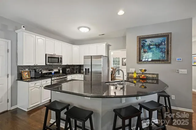a kitchen with stainless steel appliances granite countertop a dining table chairs refrigerator and microwave