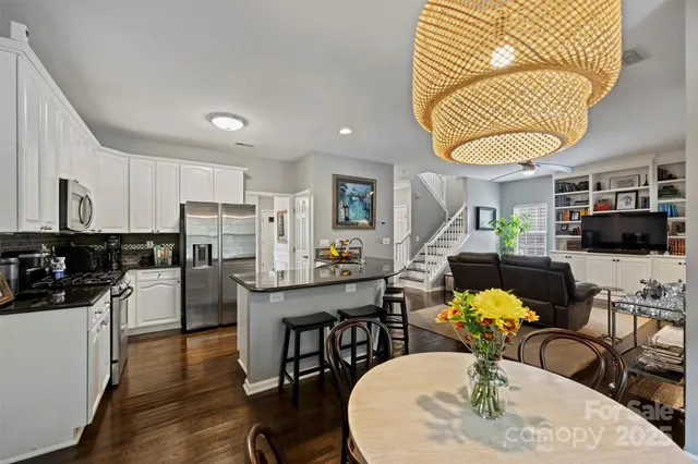 a kitchen with stainless steel appliances kitchen island granite countertop a refrigerator a stove a microwave oven a dining table and chairs with wooden floor