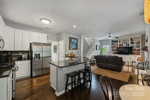 a kitchen with stainless steel appliances kitchen island granite countertop a refrigerator a stove a sink a dining table and chairs with wooden floor