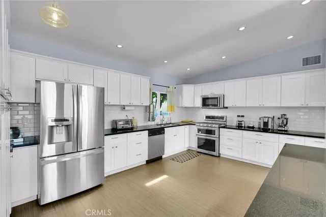 a kitchen with stainless steel appliances granite countertop a stove top oven a refrigerator a sink and white cabinets