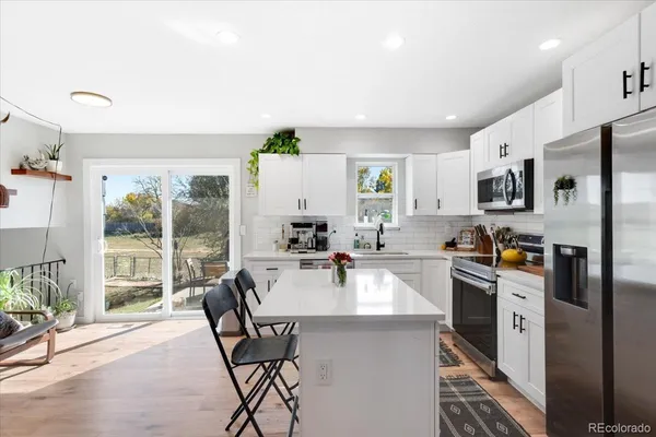 a kitchen with stainless steel appliances granite countertop a stove top oven a sink dishwasher a dining table and chairs with wooden floor