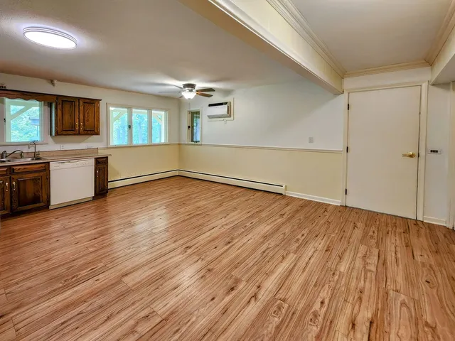 an empty room with wooden floor kitchen view and windows