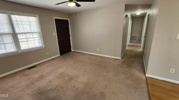 an empty room with chandelier fan and windows