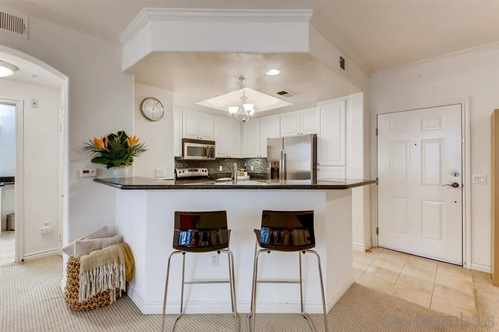 9263 Regents Road, Unit B203 La Jolla, CA 92037 - Photo 12 of 25 a kitchen with stainless steel appliances kitchen island granite countertop a dining table chairs and a refrigerator