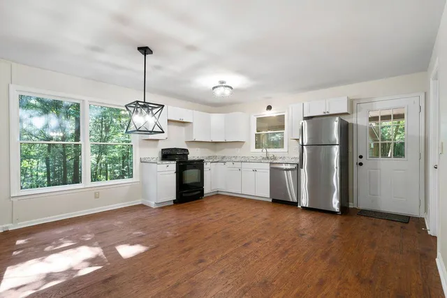 a kitchen with stainless steel appliances granite countertop a refrigerator a sink dishwasher a stove and white cabinets with wooden floor