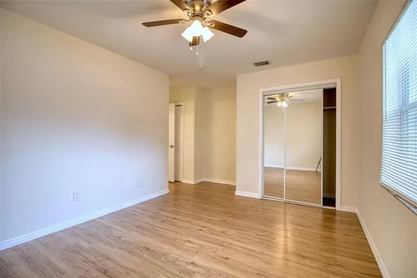 an empty room with wooden floor fan and windows