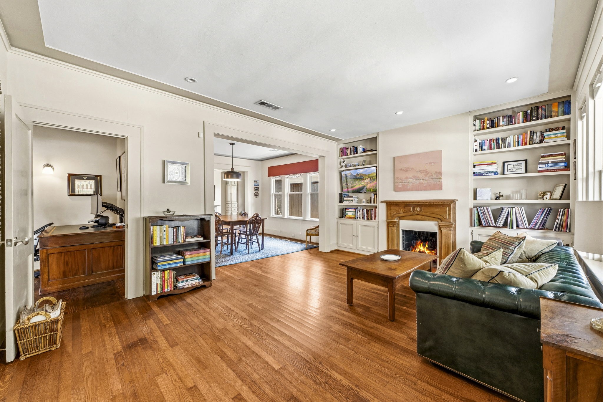 1521 Kipling Street Houston, TX 77006 - Photo 9 of 35 This cozy living room features hardwood floors, built-in bookshelves, and a fireplace. It opens to a dining area with ample natural light and includes a home office space. Perfect for comfortable living and entertaining.