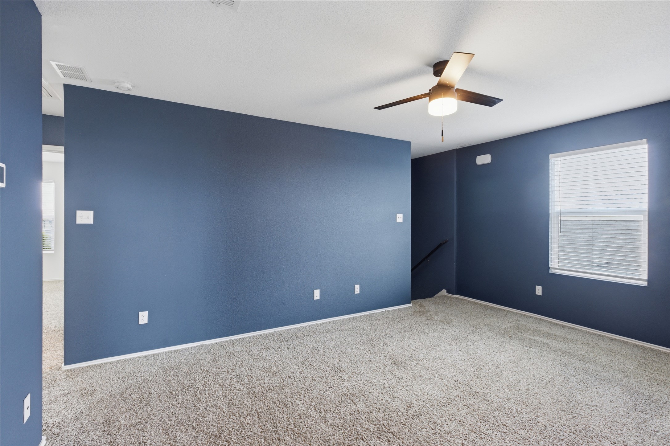 116 Night Riders Way Jarrell, TX 76537 - Photo 20 of 40 Spacious room featuring neutral carpet flooring, dark gray painted walls, a window with blinds, and a ceiling fan with integrated lighting leading to other bedrooms towards the left