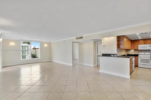 a view of an empty room with kitchen and window