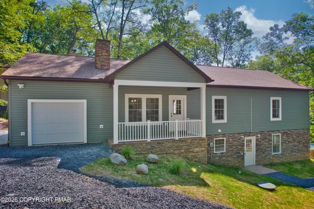 a view of a small house in front of a yard with plants and large tree