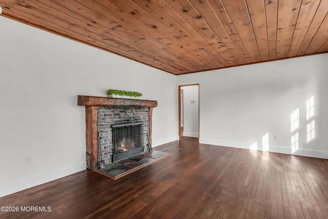 a view of an empty room with wooden floor fireplace and a window