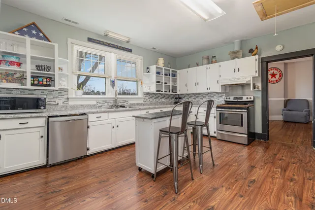 a kitchen with stainless steel appliances a stove a sink dishwasher a refrigerator with white cabinets and wooden floor