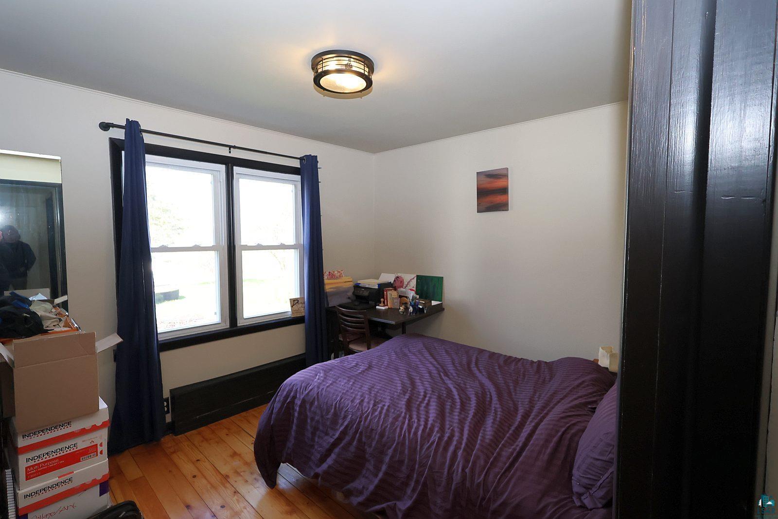 83185 Washington Avenue Port Wing, WI 54865 - Photo 15 of 26 Bright room featuring wood-finish flooring, two large windows with dark trim, a flush-mount ceiling light fixture, and light-colored walls