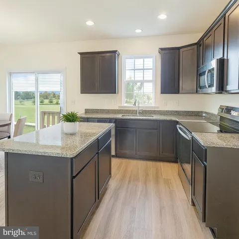a kitchen with stainless steel appliances granite countertop wooden cabinets a sink dishwasher and a stove top oven with wooden floor