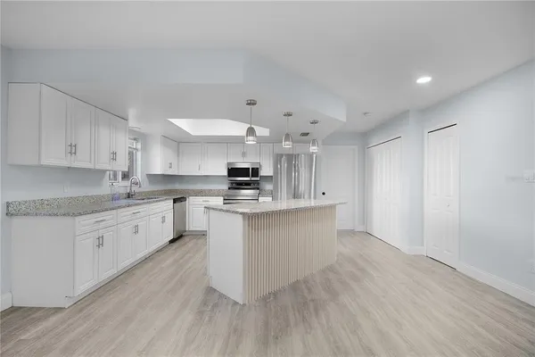 a large kitchen with kitchen island a sink dishwasher a stove a refrigerator and white cabinets with wooden floor