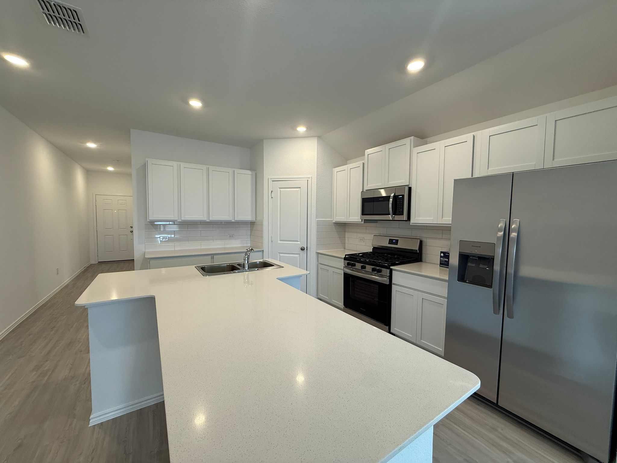 125 Sormonne Loop Kyle, TX 78640 - Photo 15 of 35 Kitchen with appliances with stainless steel finishes, a sink, light wood-style flooring, decorative backsplash, and an island with sink