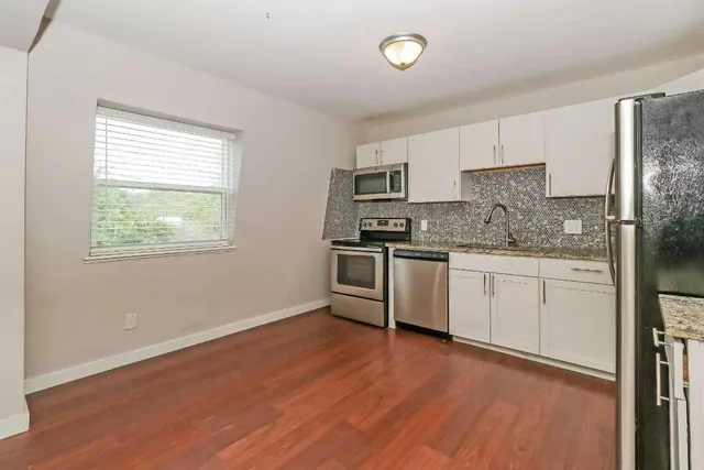 a kitchen with granite countertop wooden floors stainless steel appliances and sink