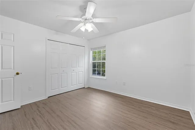 an empty room with wooden floor chandelier fan and windows