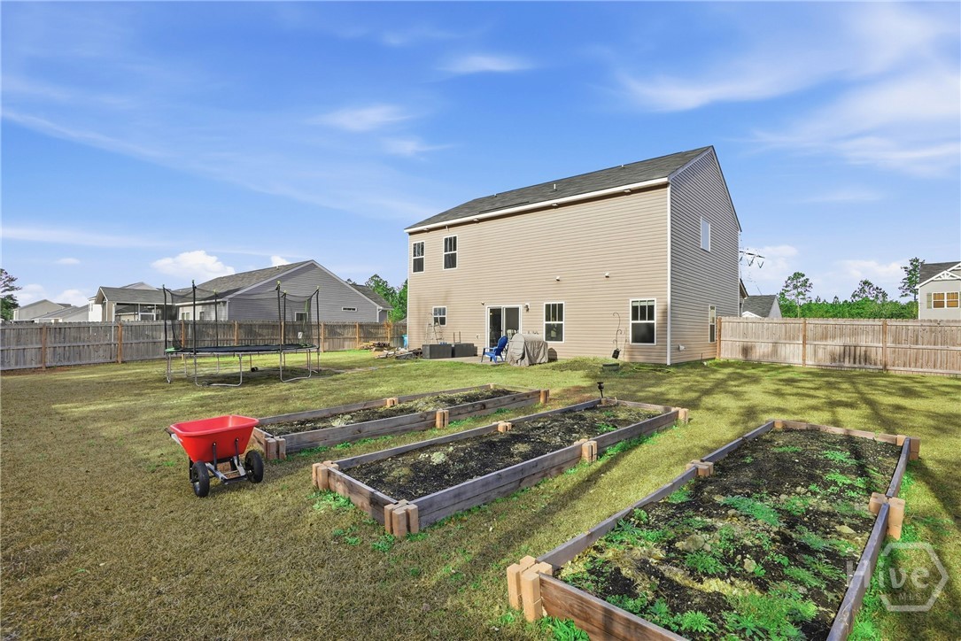 313 Crosswinds Drive Rincon, GA 31326 - Photo 33 of 34 Spacious fenced backyard with raised garden beds, dry lawn, and a two-story beige house.