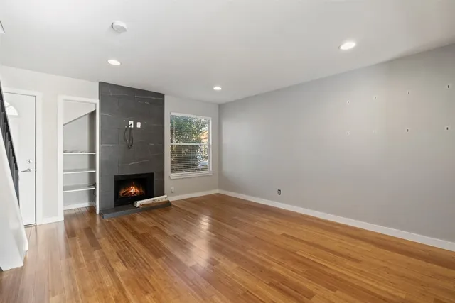 a view of an empty room with wooden floor fireplace and a window