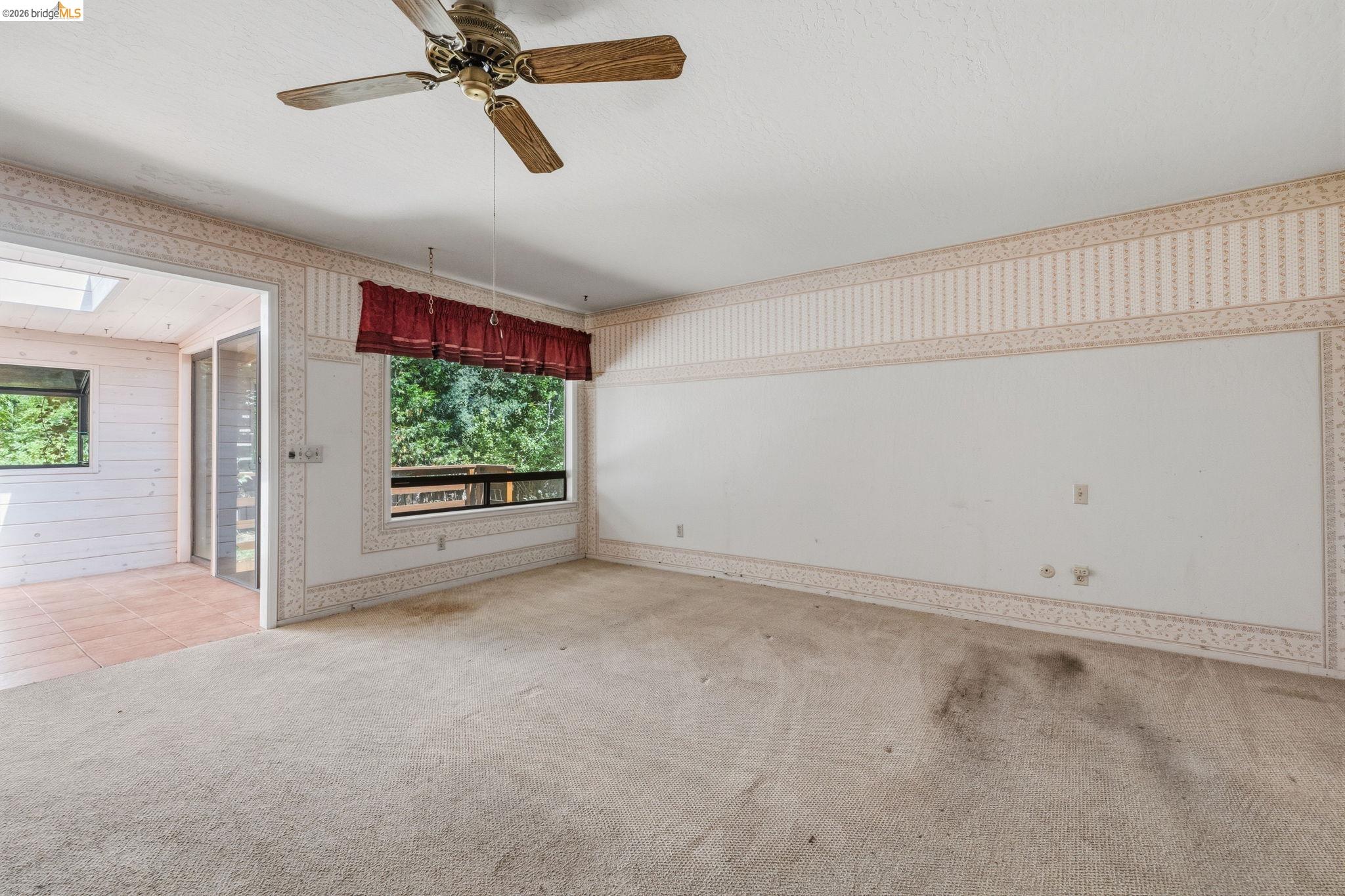 22401 South Fork Road Sonora, CA 95370 - Photo 23 of 34 Carpeted room featuring a ceiling fan with wood-finish blades, a picture window, and direct access to an enclosed sunroom with skylights and terra cotta-style floor tiles