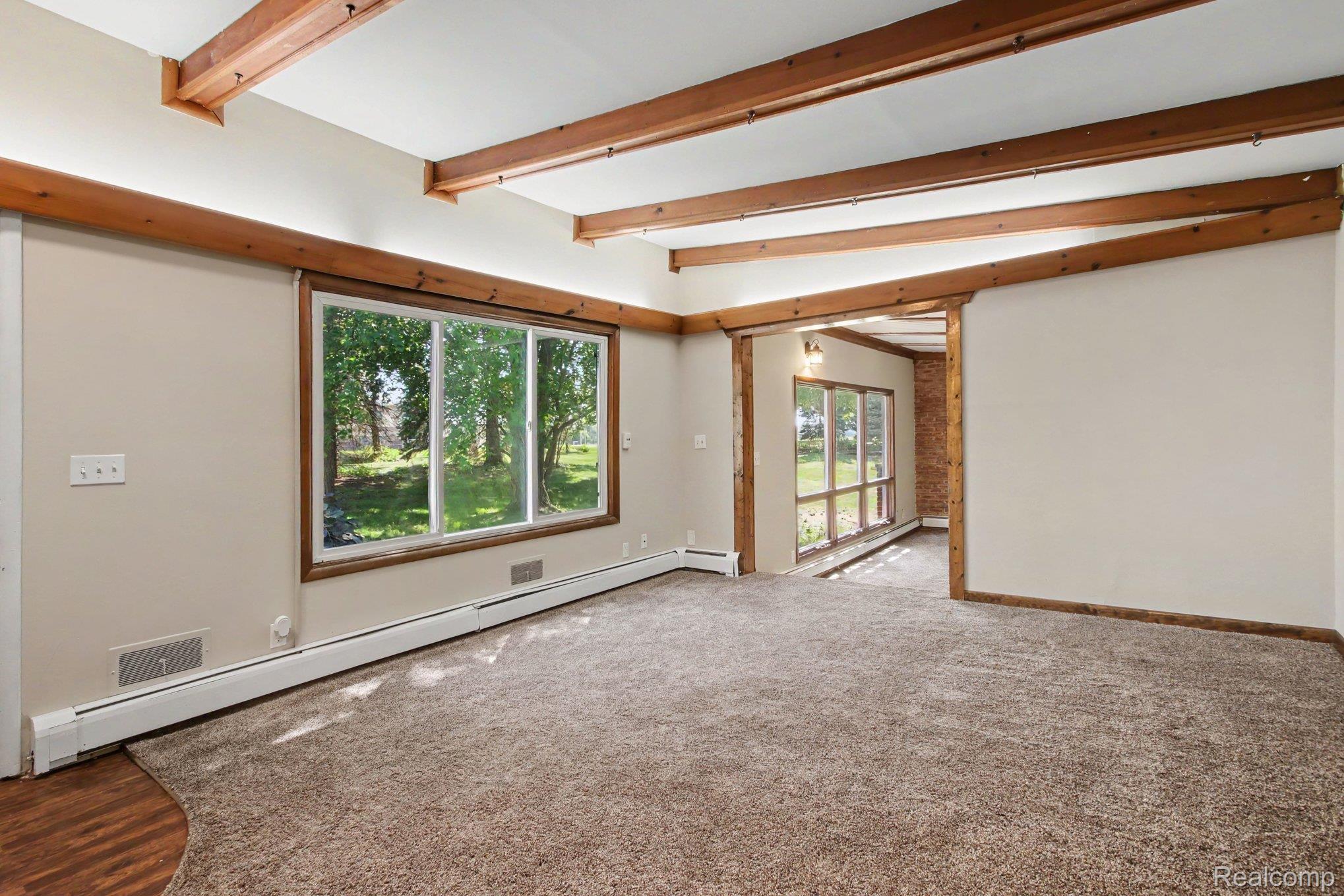 7800 Sharpe Road Fowlerville, MI 48836 - Photo 6 of 22 Expansive room featuring exposed wood ceiling beams, a large picture window, light-colored walls, and neutral carpeting