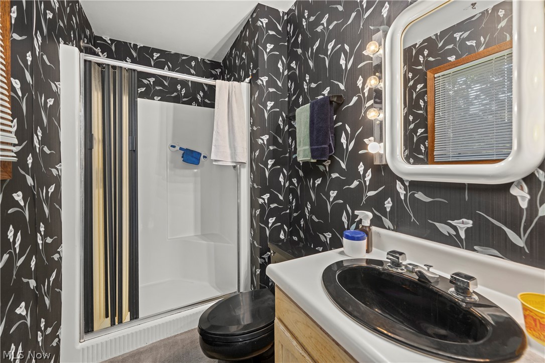 6451 Kungle Road Clinton, OH 44216 - Photo 26 of 34 Contemporary bathroom featuring bold geometric patterned wallcovering, a sleek oval vessel sink with wood-finish vanity, frameless rounded mirror with integrated lighting, and a walk-in shower enclosure with white subway tile surround and sliding glass door