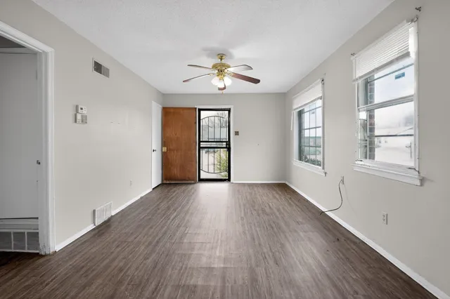 an empty room with wooden floor chandelier fan and windows