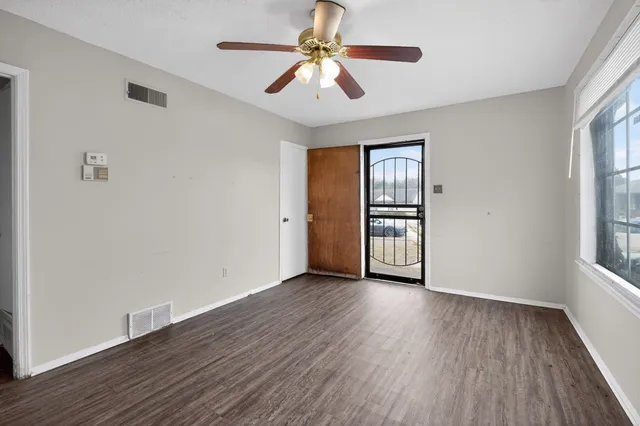 an empty room with wooden floor chandelier fan and windows