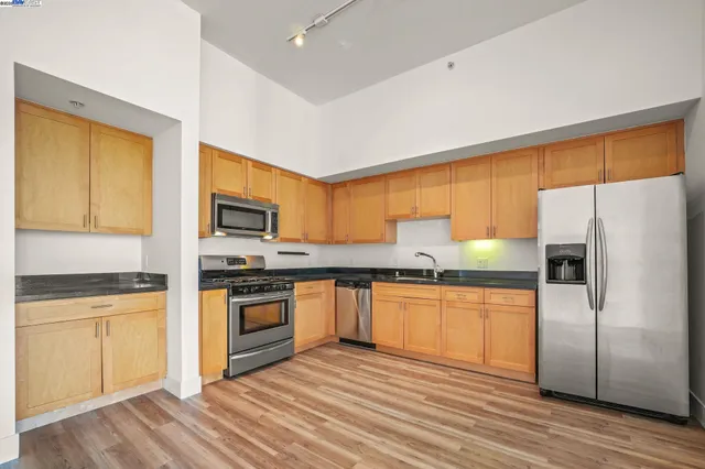 a kitchen with stainless steel appliances granite countertop a stove top oven a refrigerator and white cabinets with wooden floors