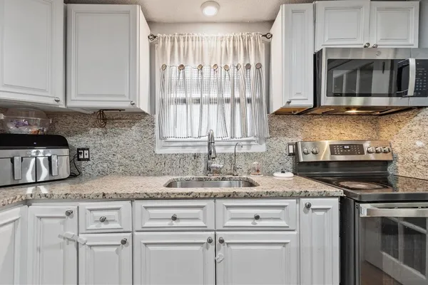 a kitchen with granite countertop white cabinets and black stainless steel appliances