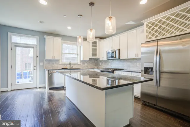 a kitchen with stainless steel appliances granite countertop a refrigerator a sink dishwasher a stove and white countertops with wooden floor