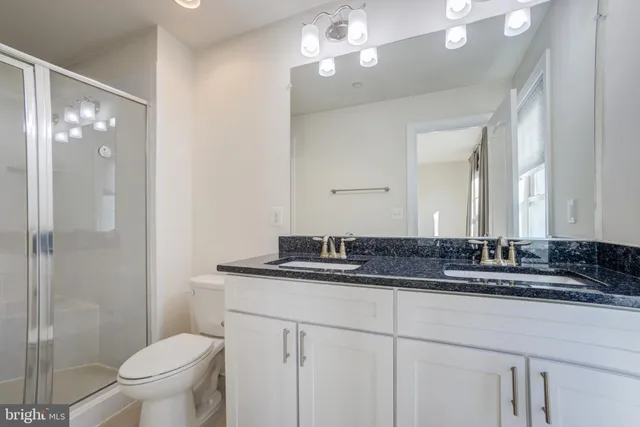 a bathroom with a granite countertop sink a toilet a mirror and shower