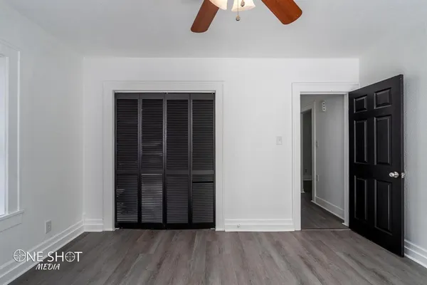 an empty room with wooden floor closet and windows