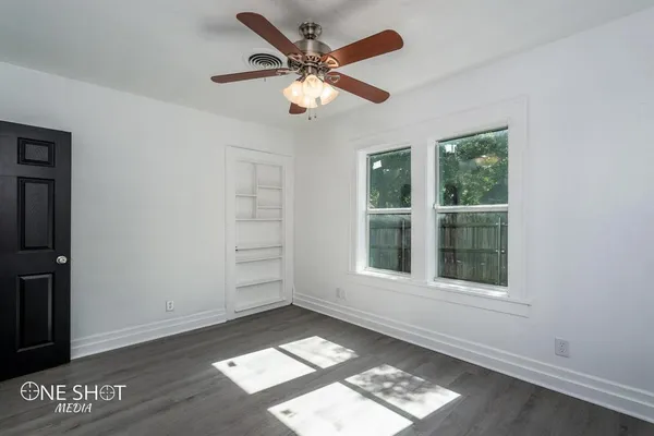 an empty room with wooden floor cabinet and windows