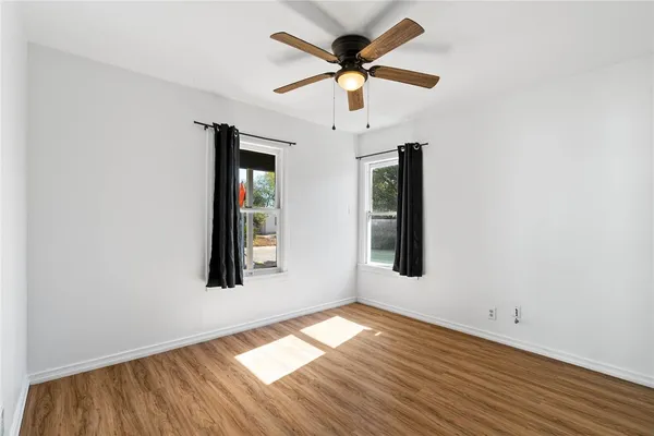 an empty room with wooden floor chandelier fan and windows
