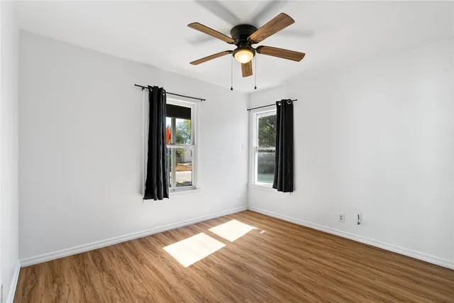 an empty room with wooden floor chandelier fan and windows