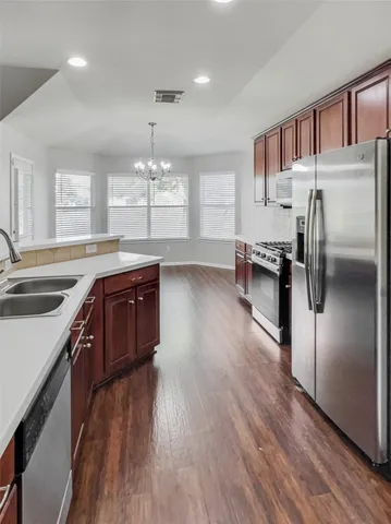 a kitchen with stainless steel appliances granite countertop a refrigerator a sink dishwasher a stove and white countertops with wooden floor