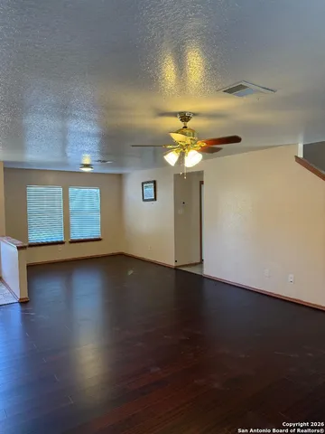 an empty room with wooden floor chandelier fan and windows