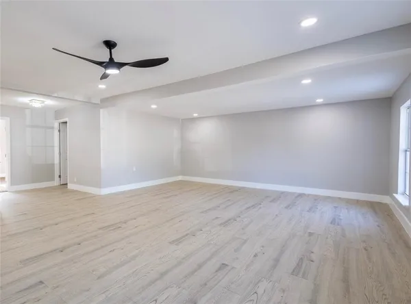 a view of an empty room with wooden floor and a ceiling fan