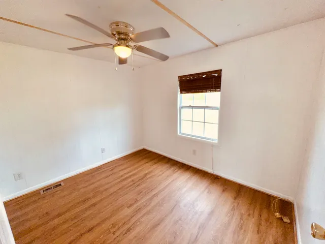 an empty room with wooden floor chandelier fan and windows