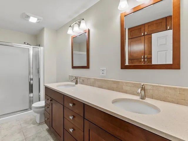 a bathroom with a double vanity sink and mirror with toilet