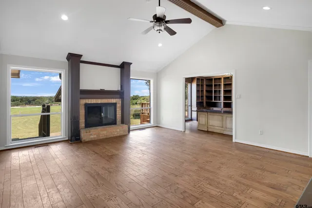 an empty room with wooden floor fireplace and windows