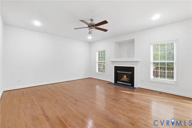 a view of an empty room with wooden floor fireplace and a window