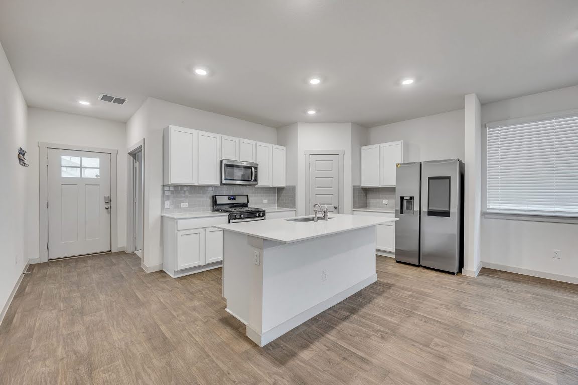 210 Big Cypress Bayou Road Hutto, TX 78634 - Photo 5 of 27 Kitchen with stainless steel appliances, white cabinets, a center island with sink, light wood-style floors, and recessed lighting